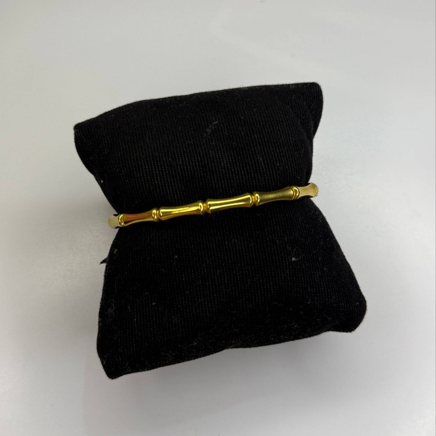 Gold bracelet on a black pillow against a white background
