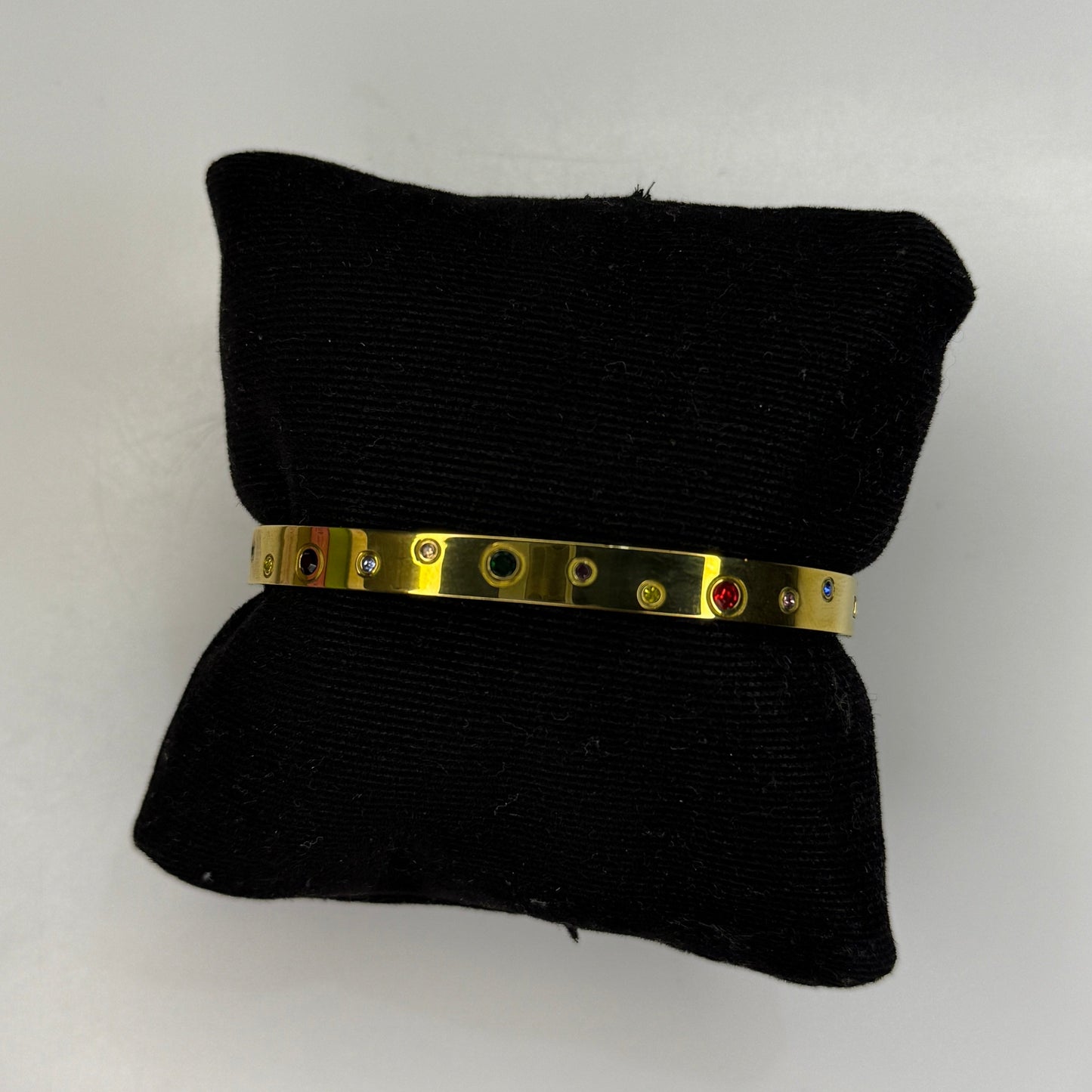 Gold bracelet on a black pillow against a white background