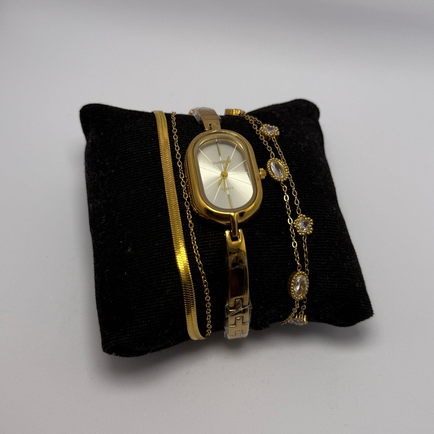 Gold bracelet with a watch face on a black cushion against a white background