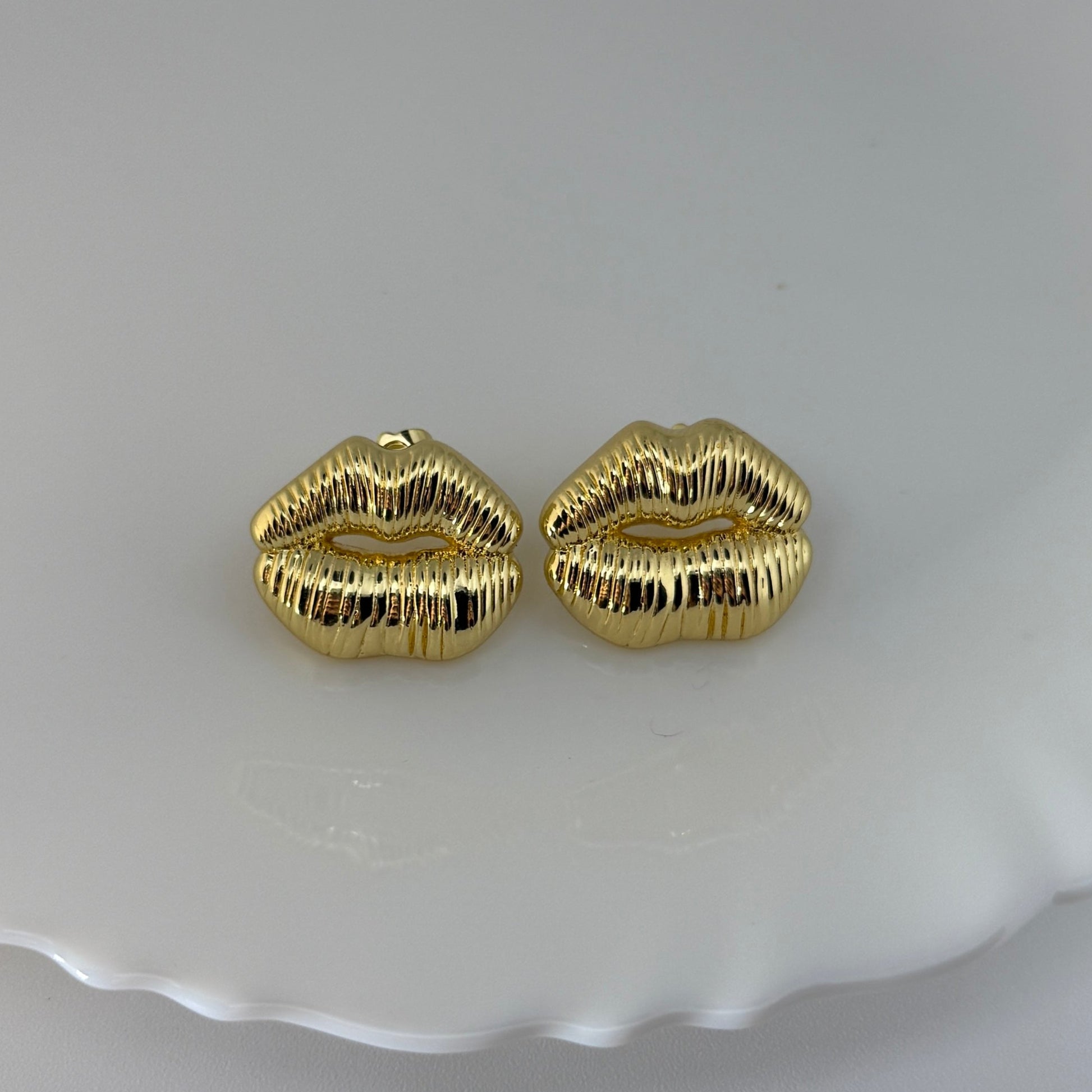 Gold lip-shaped earrings on a white dish