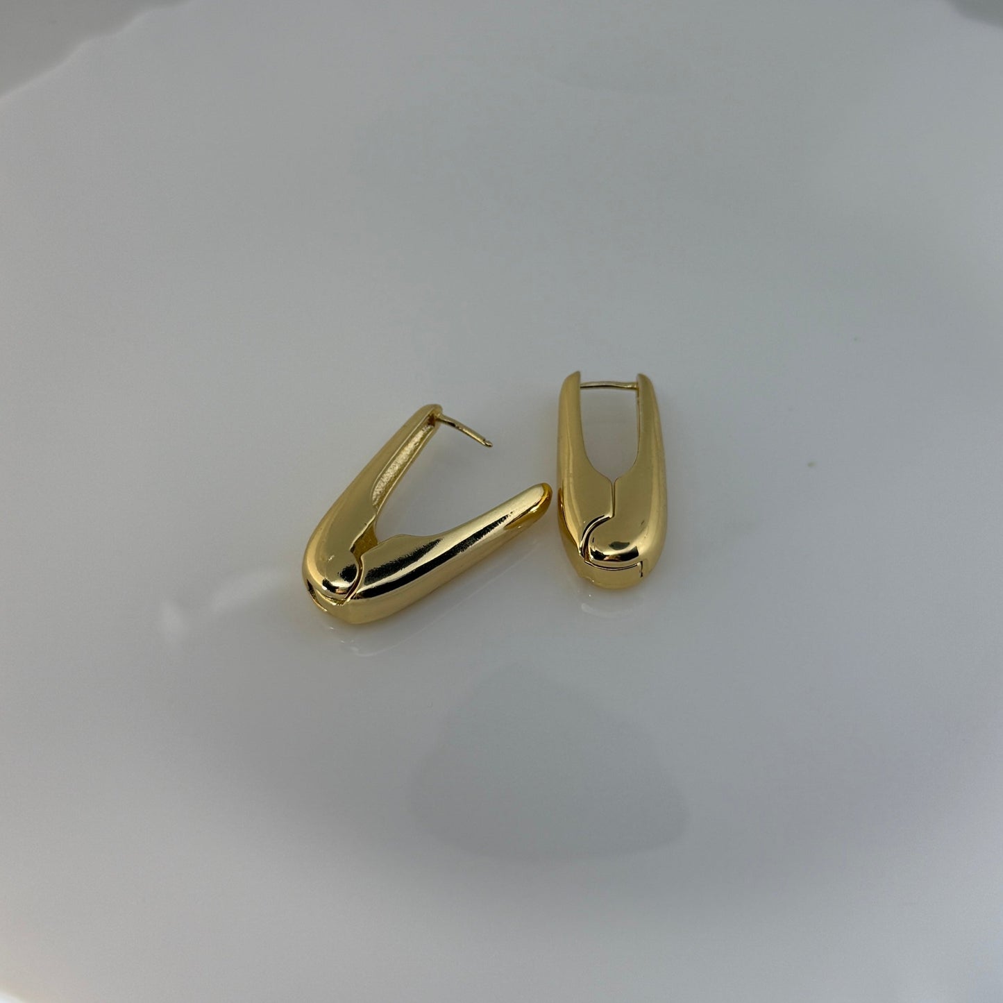 Pair of gold hoop earrings on a white ceramic plate