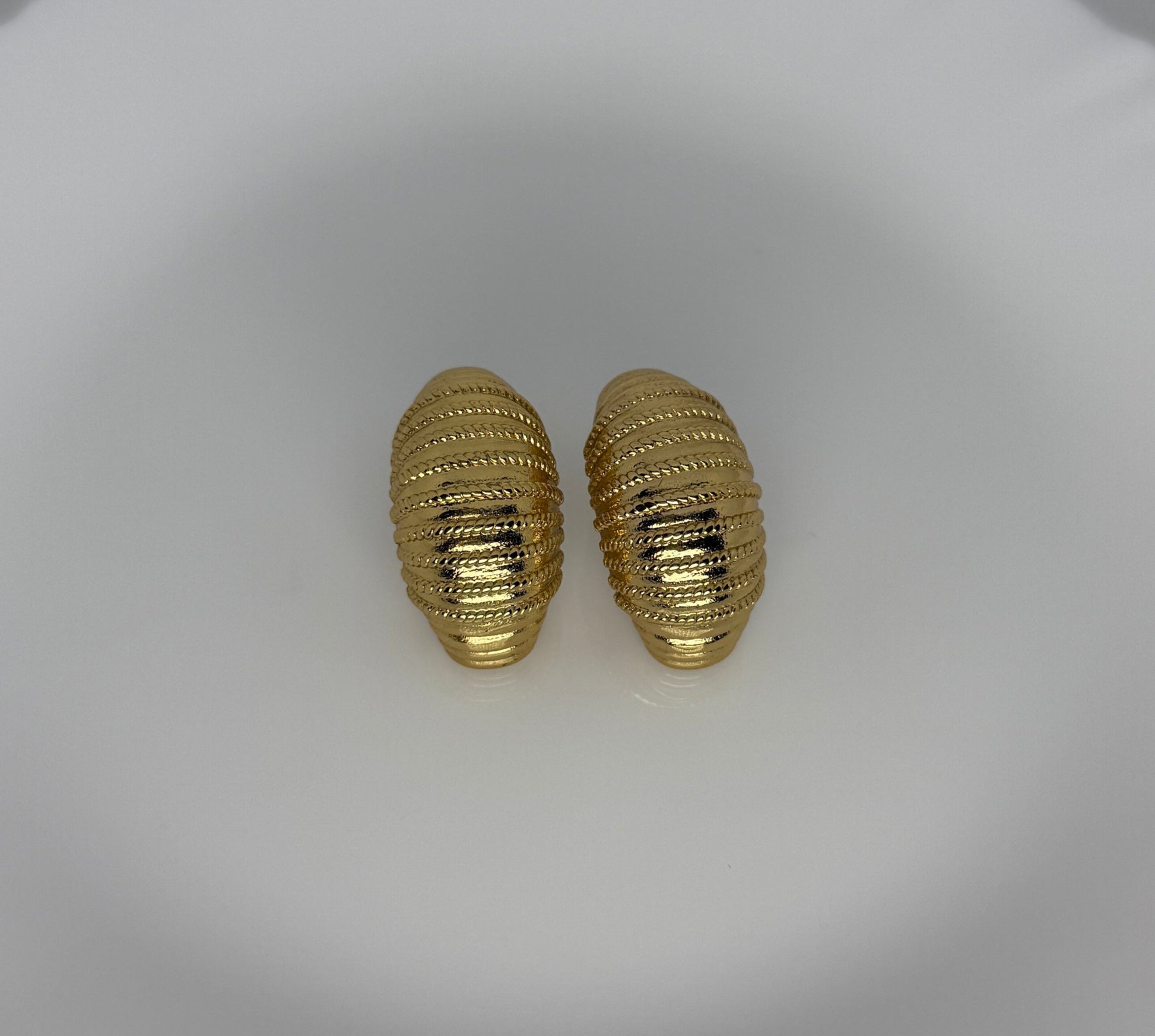 Pair of gold textured earrings on a white dish
