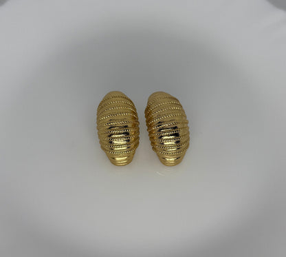Pair of gold textured earrings on a white dish