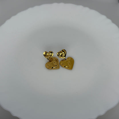 Gold heart-shaped earrings on a white cushion with a blurred background