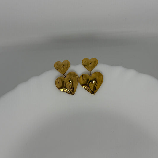 Gold heart-shaped earrings on a white stand against a gray background