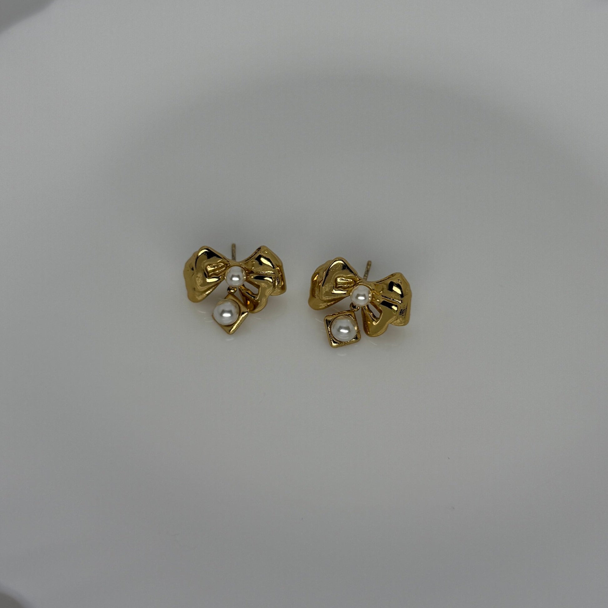Gold bow-shaped earrings with pearl centers on a white plate.