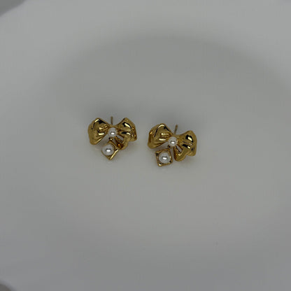 Gold bow-shaped earrings with pearl centers on a white plate.