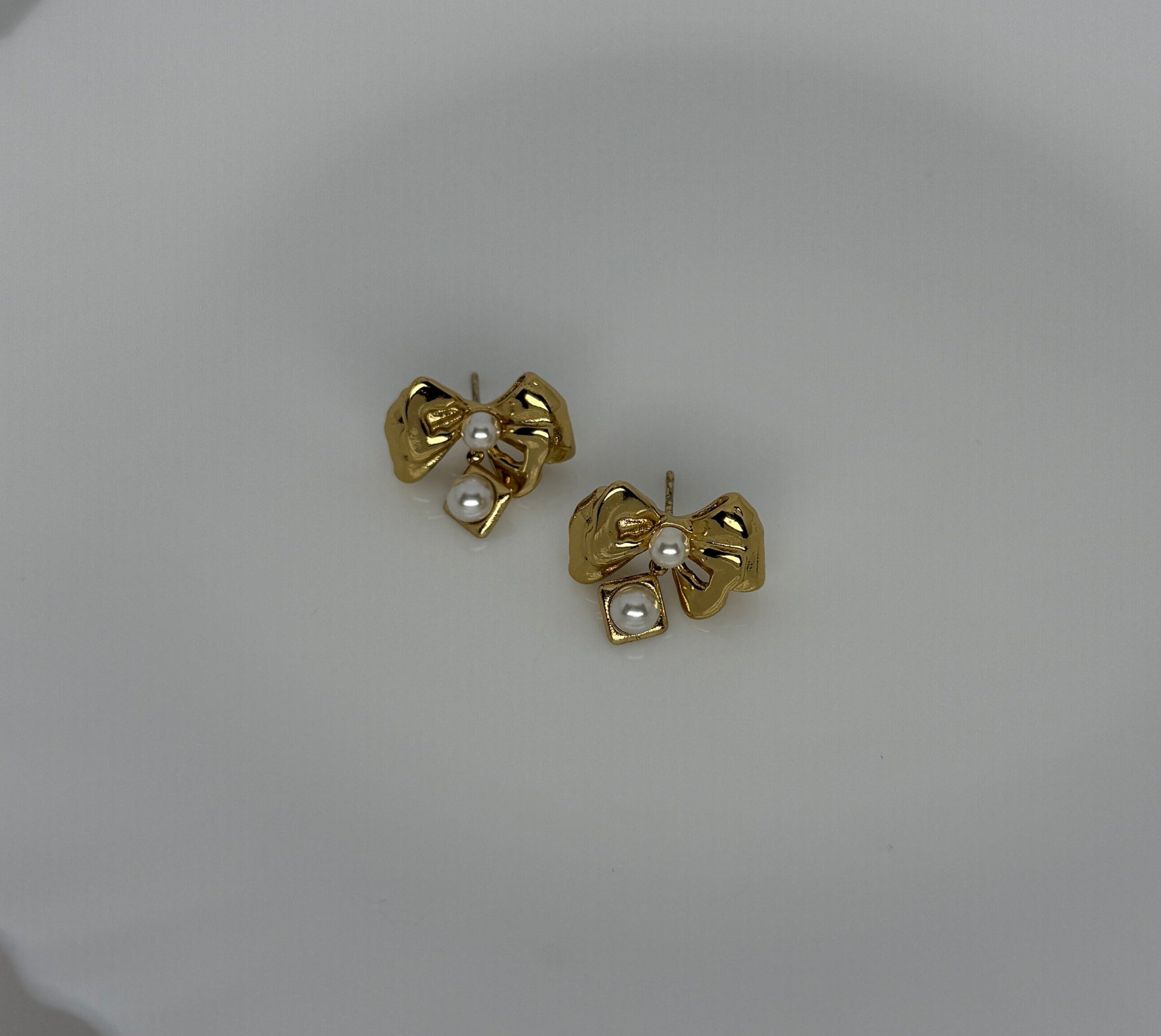 Gold bow-shaped earrings with pearl centers on a light gray background