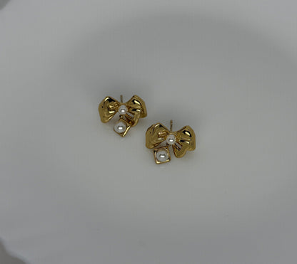Gold bow-shaped earrings with pearl centers on a light gray background