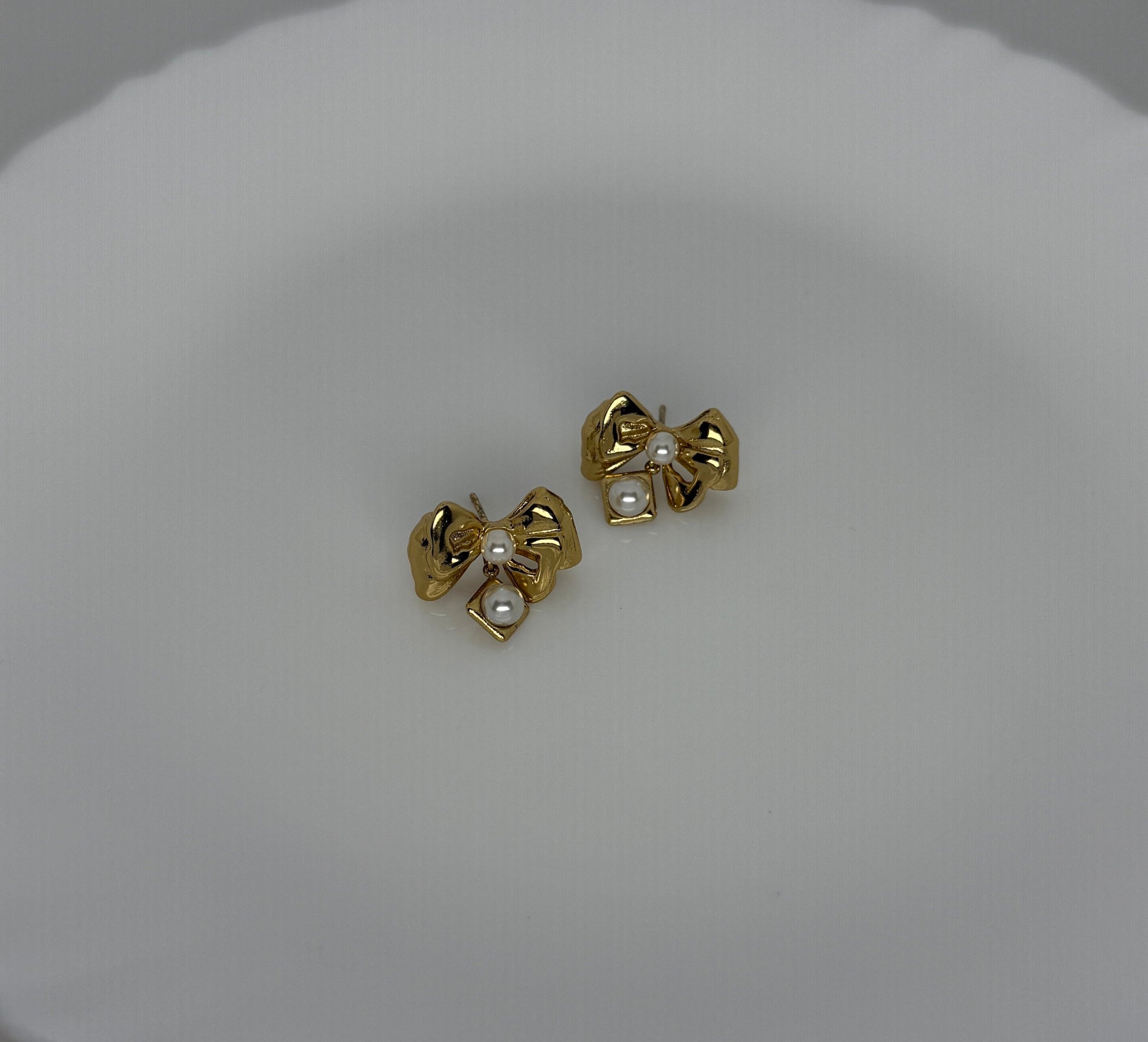 Gold bow-shaped earrings with pearl centers on a white background