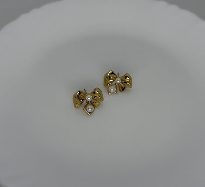 Gold bow-shaped earrings with pearl centers on a white background