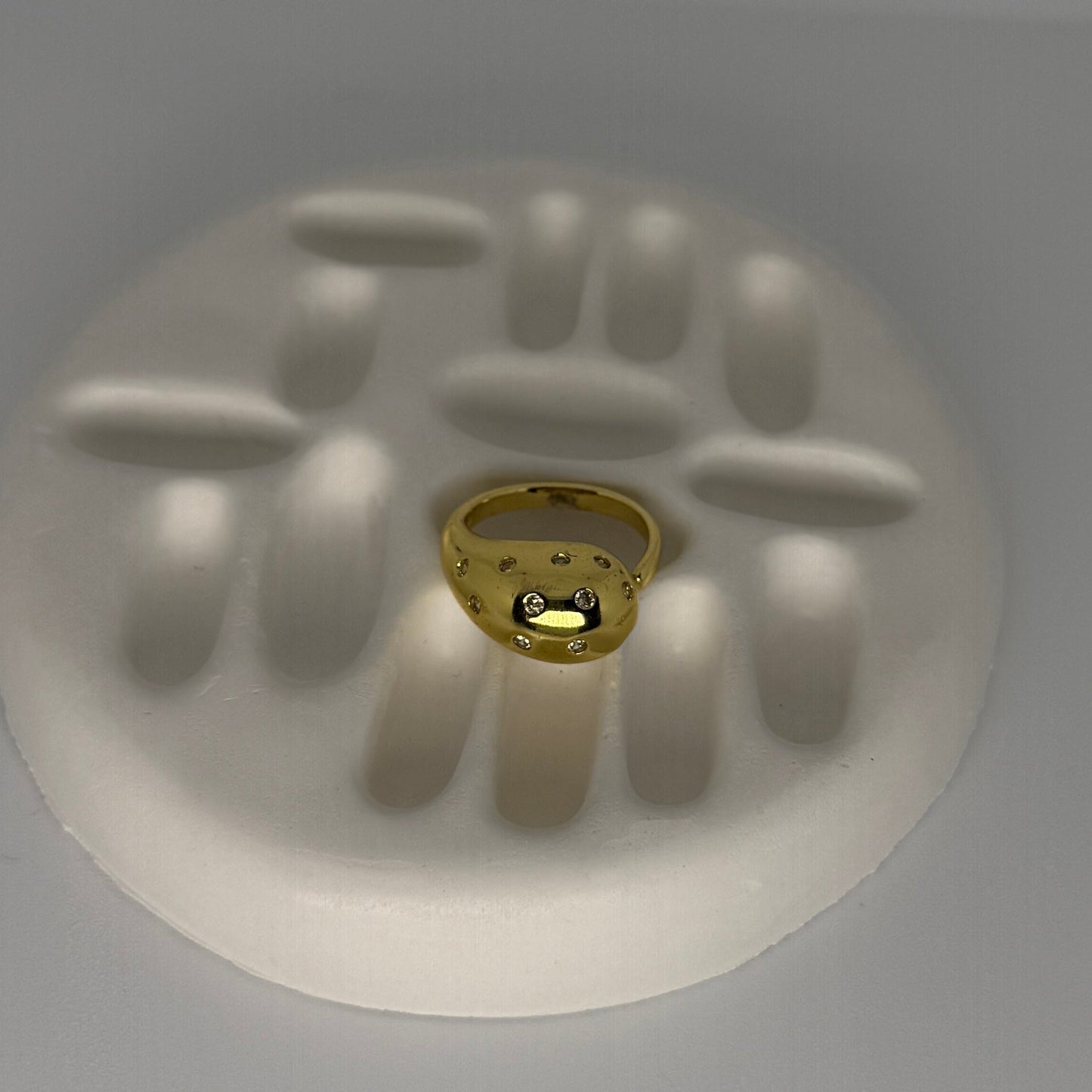 Gold ring with embedded stones on a white handprint mold against a gray background