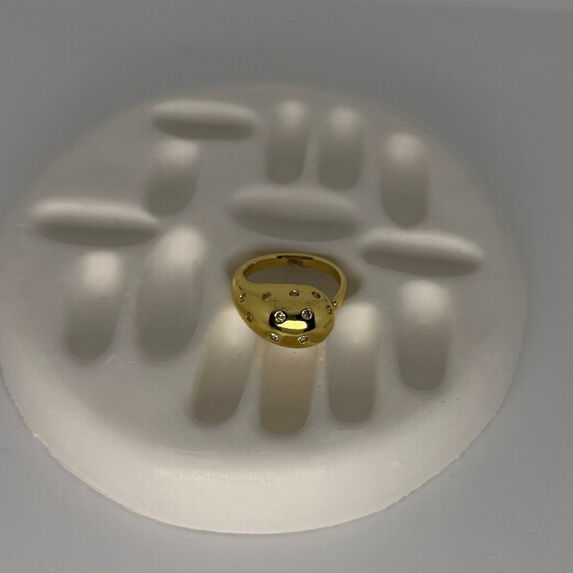 Gold ring with embedded stones on a white handprint mold against a gray background