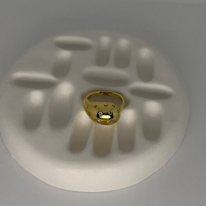 Gold ring with embedded stones on a white handprint mold against a gray background