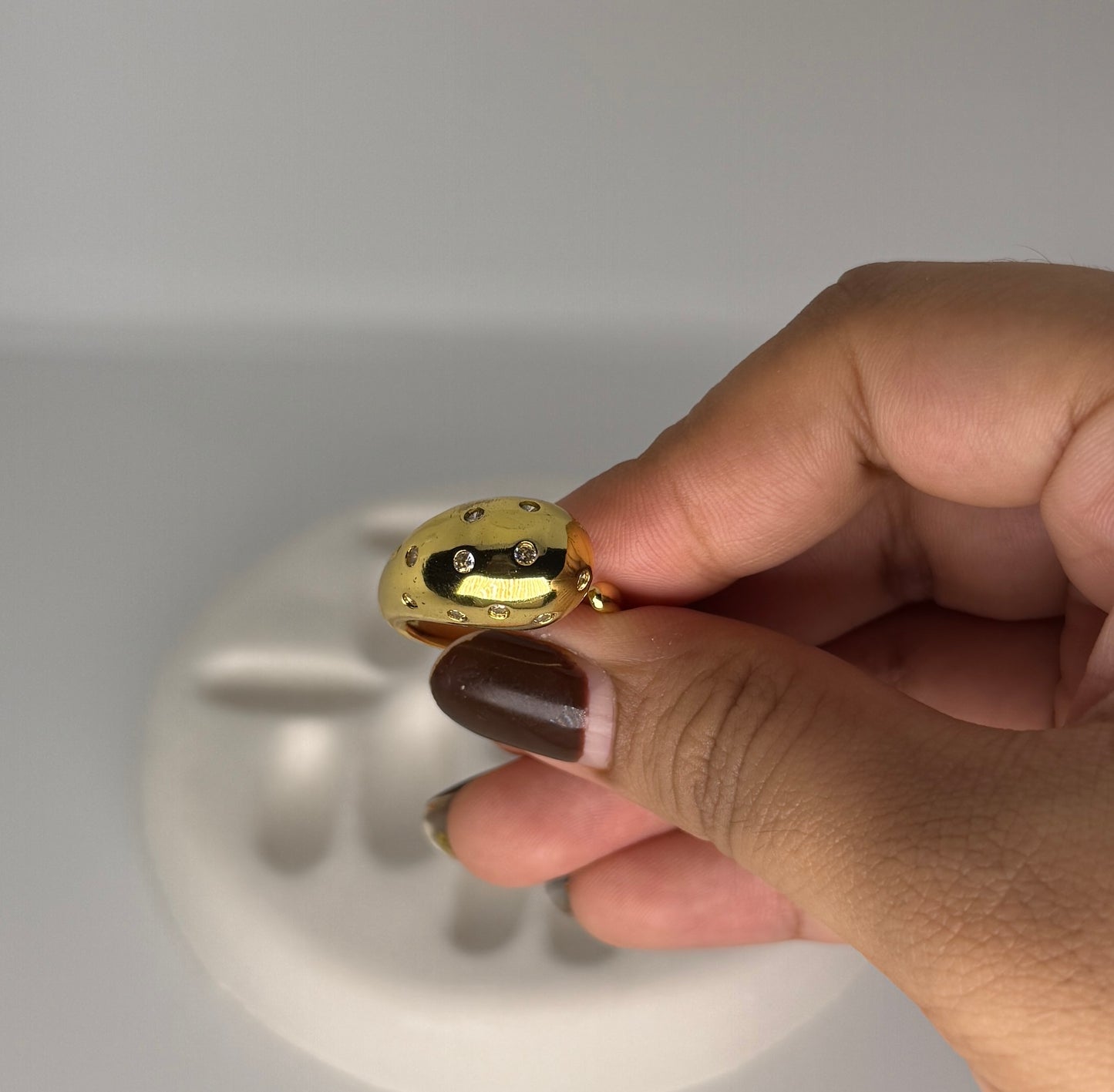 Gold ring with embedded stones held by a hand against a neutral background