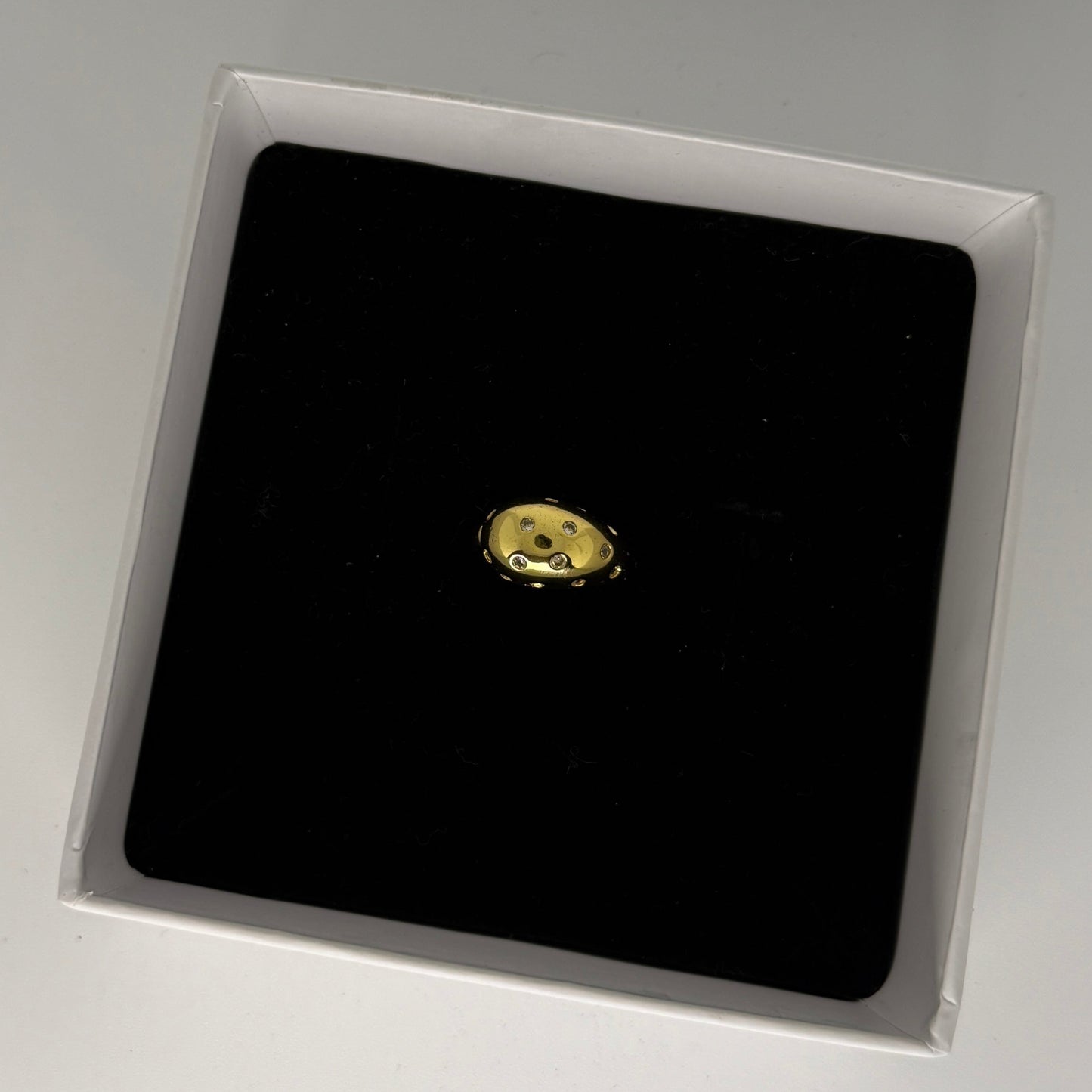 Gold earring on a black square in a clear box on a gray background