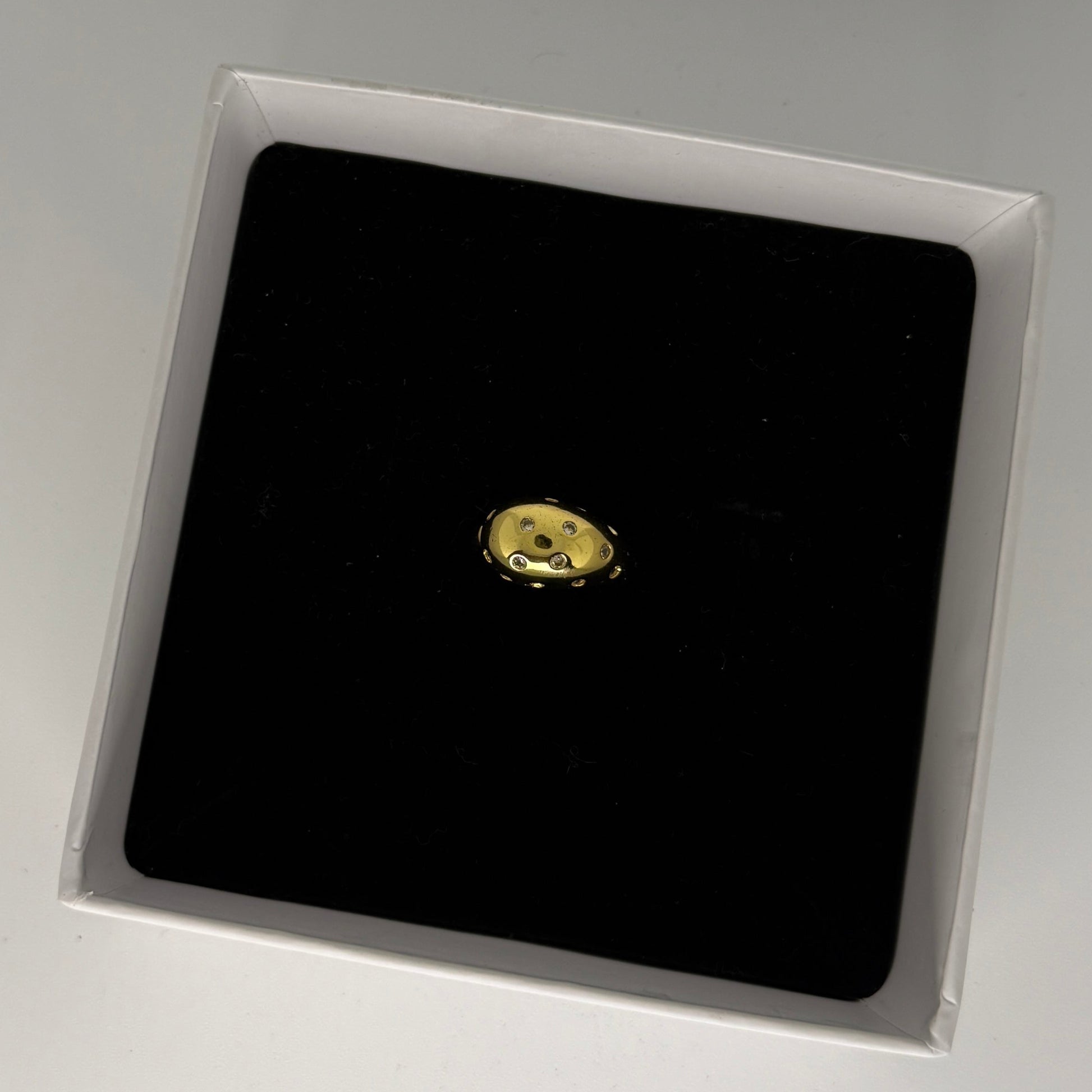 Gold earring on a black square in a clear box on a gray background