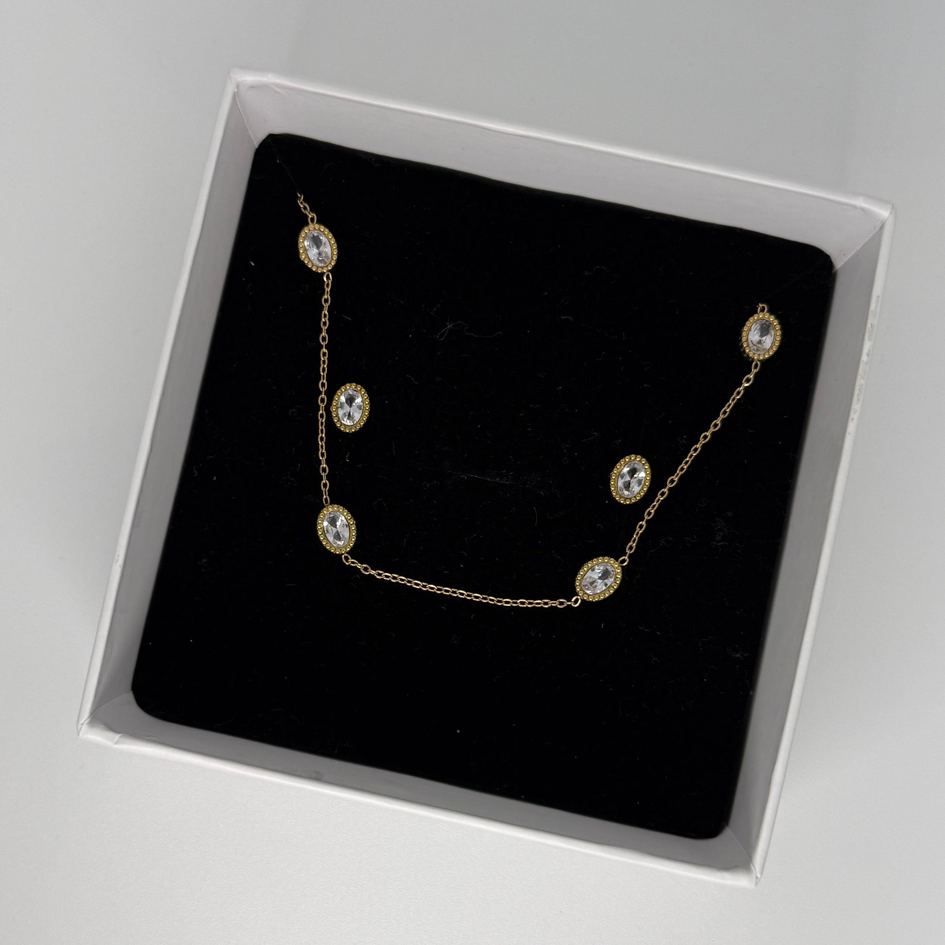 Gold necklace with clear stones in a black box on a gray background
