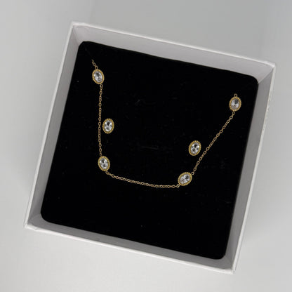 Gold necklace with clear stones in a black box on a gray background